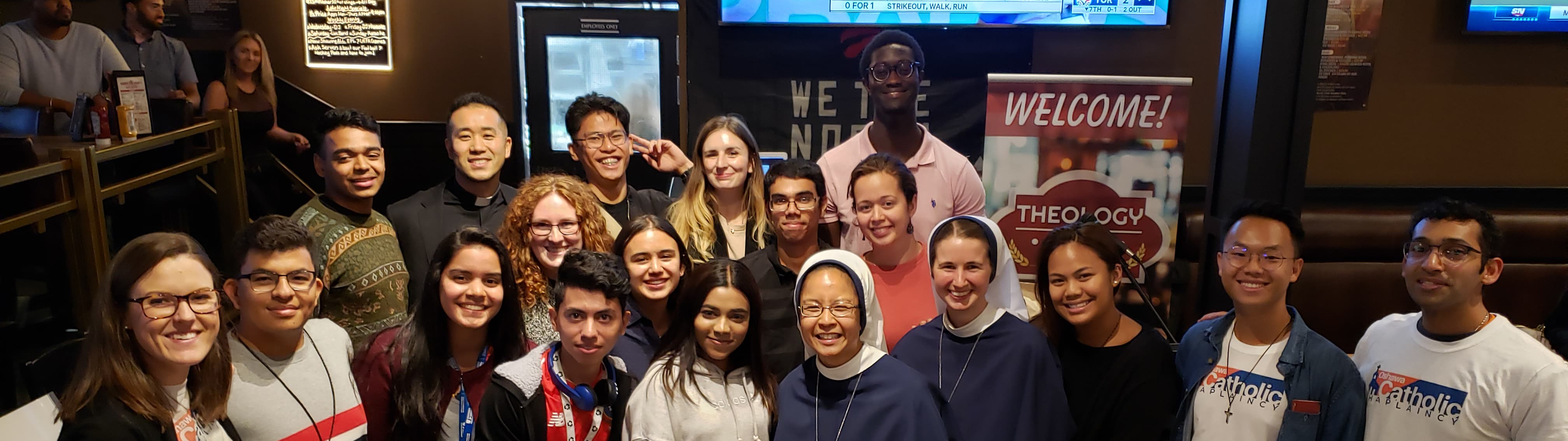 Group of male and female young adults with a few nuns gathered inside a pub/restaurant smiling for a photo